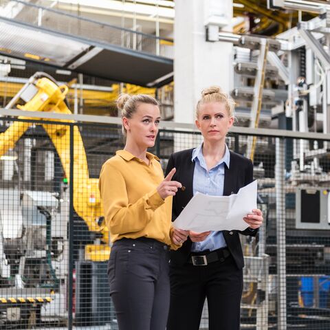 Deux femmes discutent d'un projet dans l'atelier d'une usine, en présence d'un robot industriel