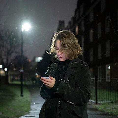 Una persona con i capelli castani si trova di notte nella neve, avvolta in un cappotto, e guarda concentrato il suo smartphone.