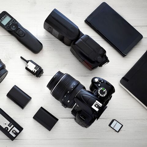 Photo equipment on a white table: DSLR camera, lenses, flash, microphone, remote shutter release, memory cards, batteries and a tablet.