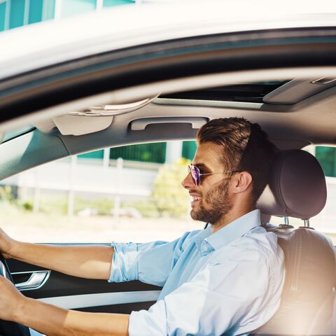 Ein Mann in Business Casual Outfit mit einer Sonnenbrille sitzt im Auto.