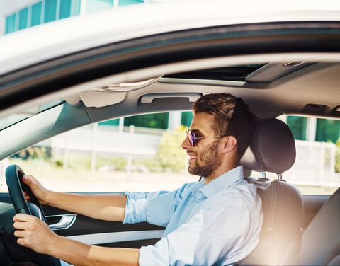 Ein Mann in Business Casual Outfit mit einer Sonnenbrille sitzt im Auto.
