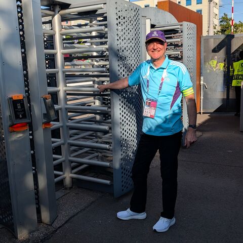 An AXA employee in a volunteer shirt stands in front of the turnstile of the stadium.