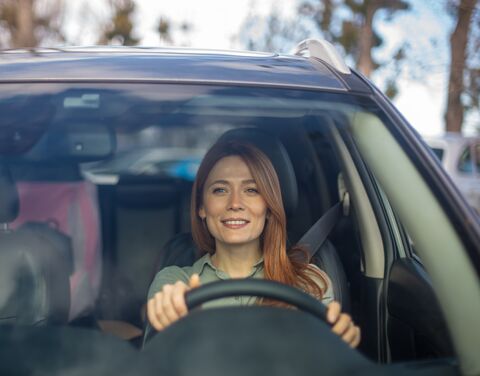 Una donna sorridente guida un’auto.