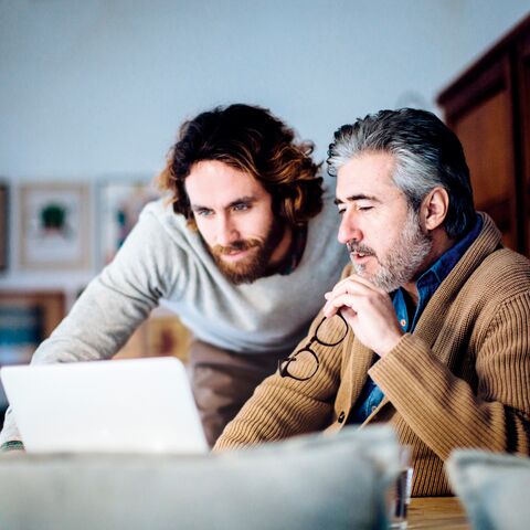 Due uomini lavorano insieme a un computer portatile, uno tiene un paio di occhiali mentre l'altro si guarda alle spalle.