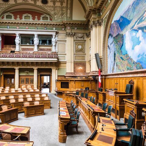 An empty meeting room with wooden tables and chairs, decorated with statues, a clock and a large mural with a landscape motif.