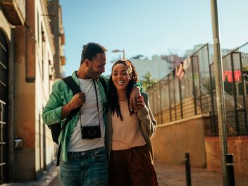 Donna e marito sono in vacanza e corrono ridendo per strada. 
