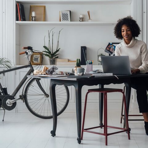 Una giovane donna siede a un tavolo nero e lavora al laptop. Alla sua destra c’è una bicicletta.