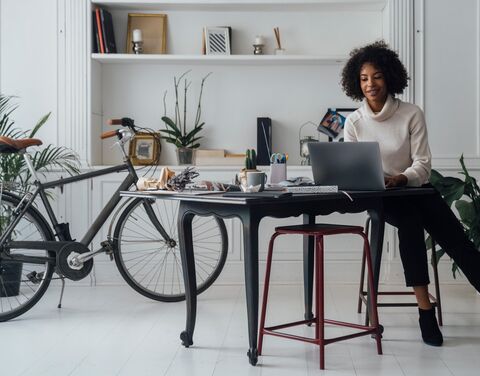 Une jeune femme est assise à une table noire et travaille sur son ordinateur portable. À sa droite se tient un vélo.