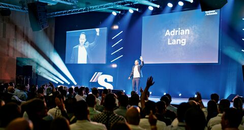 Adrian Lang steht auf einer Bühne und wird vom Publikum beklatscht.