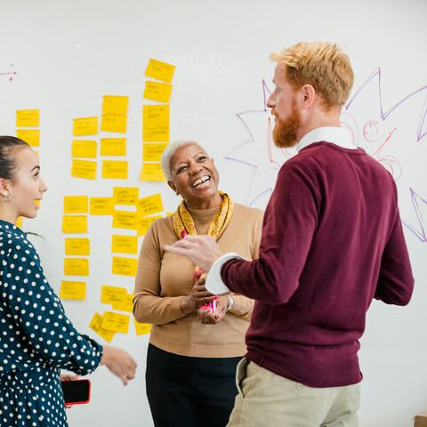 Quatre collaborateurs discutent devant un tableau blanc couvert de post-it jaunes.