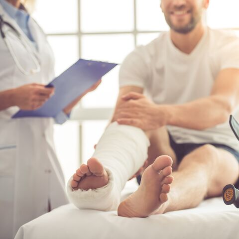 Un uomo giace sul letto da visita presso il medico. La gamba è intonacata e le stampelle appoggiate al letto.