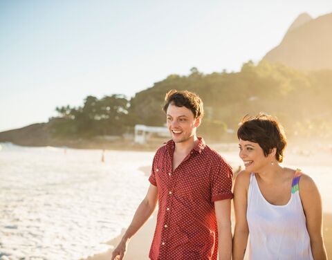Ein Pärchen macht Urlaub in Brasilien und spaziert in der Abendsonne der Küste entlang. 