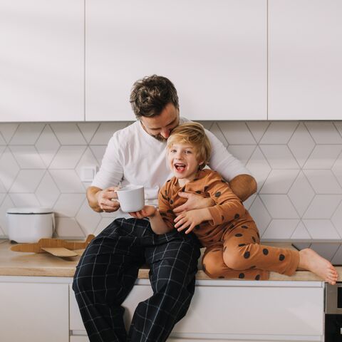 Un père et son enfant sont dans la cuisine en train de rire.