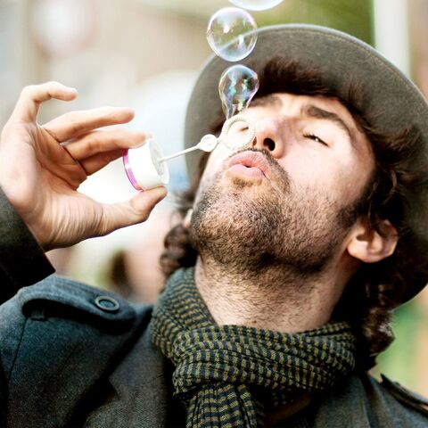 A young man dressed in winter blows soap bubbles into the air.