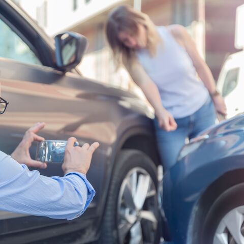 Un jeune homme se tient au bord de la route à côté de sa voiture et regarde son smartphone.