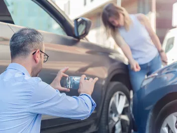 Una donna e un uomo fotografano e osservano un danno da collisione.