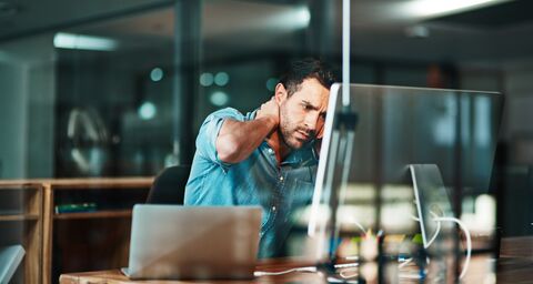Un homme épuisé est assis à son bureau devant son ordinateur portable et se tient la nuque.