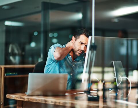 Un homme épuisé est assis à son bureau devant son ordinateur portable et se tient le front.