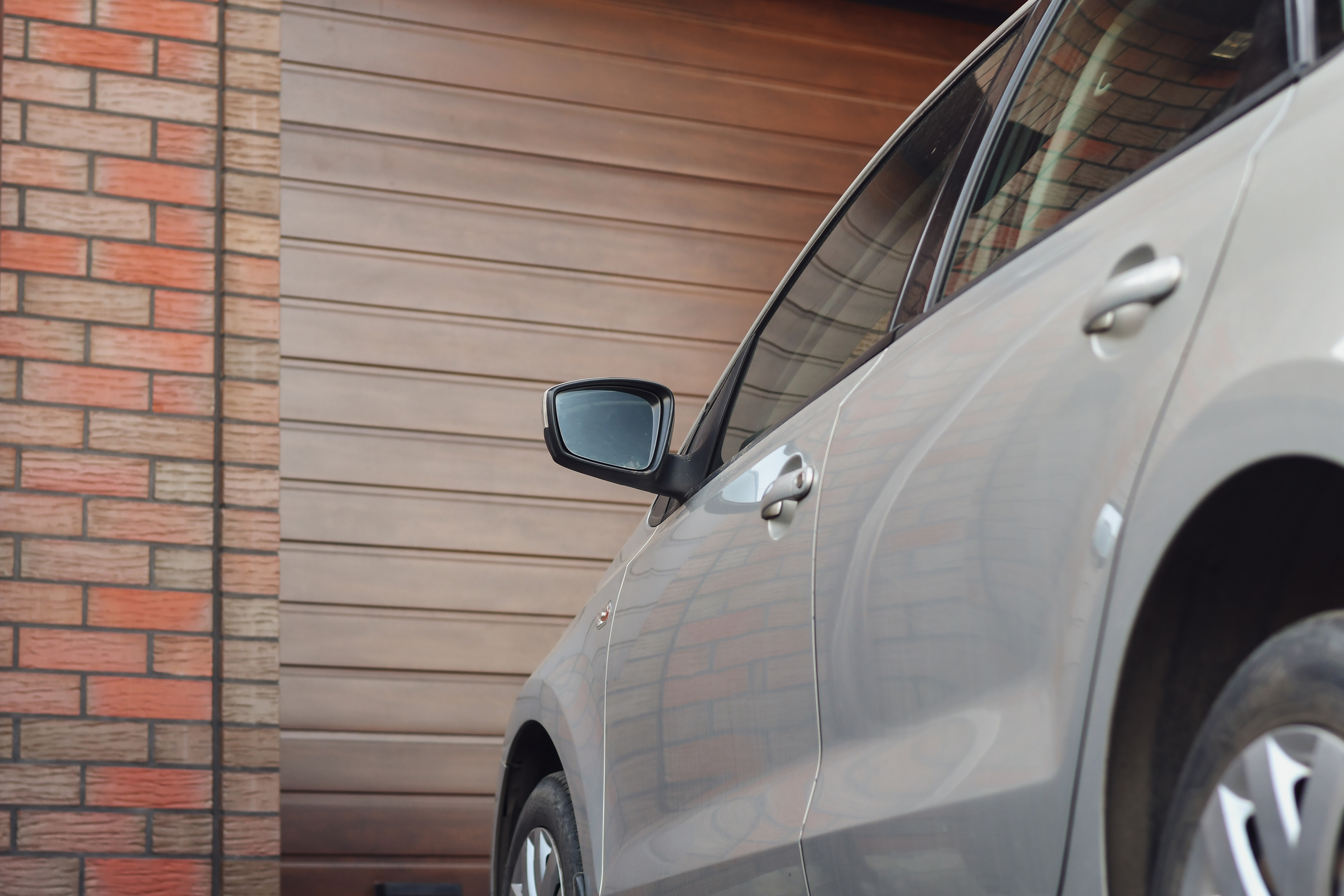 Un’auto color argento parcheggia davanti a una porta di garage in legno chiusa accanto a un muro di mattoni.