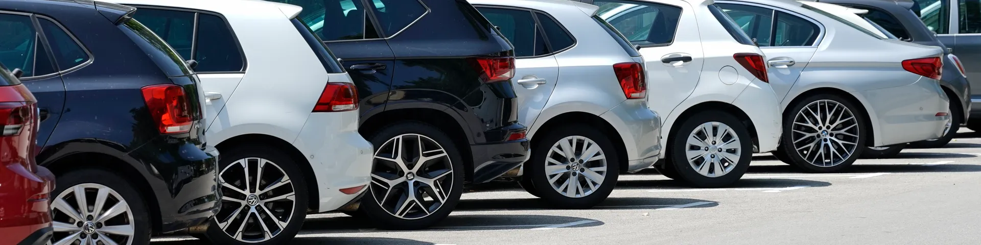 Eine Reihe von geparkten Autos in verschiedenen Farben steht nebeneinander auf einem Parkplatz an einem sonnigen Tag.