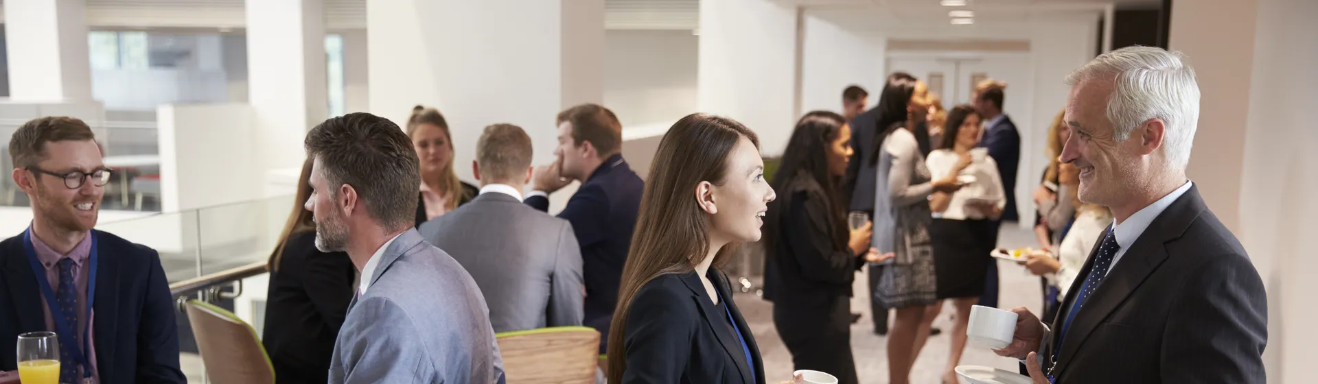 People in business attire chat over drinks and snacks during a networking event in a modern office building.