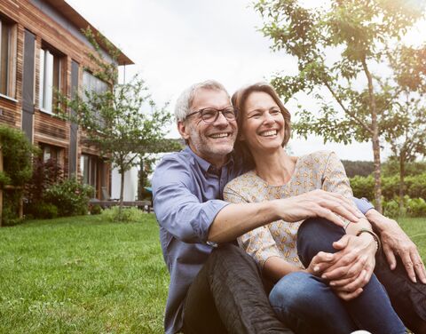 Couple sitting leaning against each other in front of their house