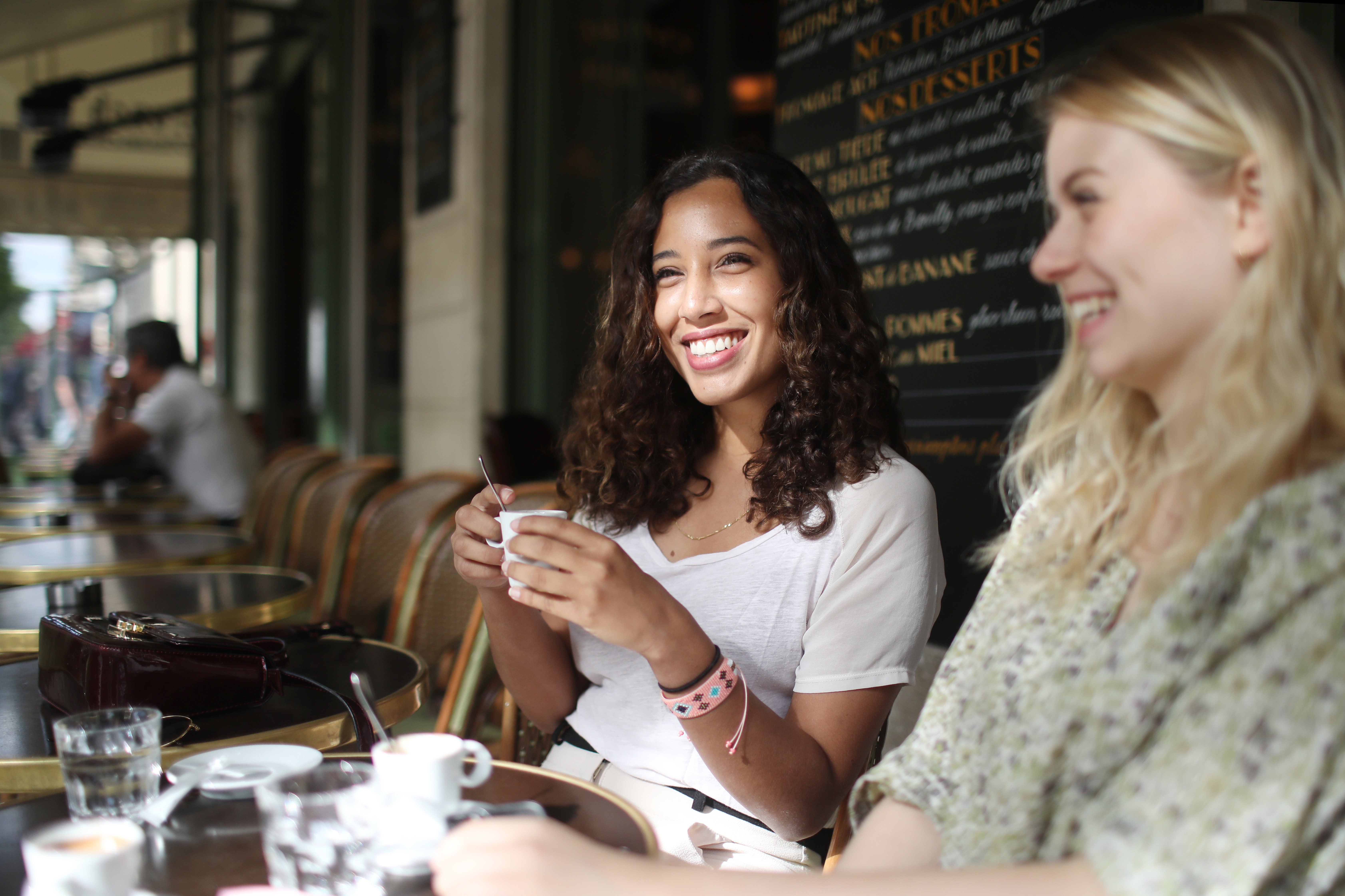 Two young women are sitting in a café and drinking a hot drink together.