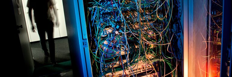Silhouette eines Mannesn eben einem Server mit Kabeln