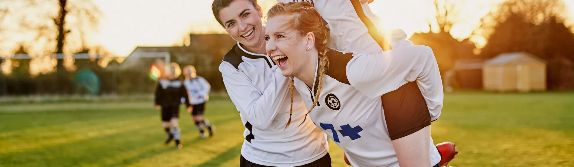 Un gruppo di donne sorridenti festeggia insieme all'aperto, una donna viene portata in spalla dalle altre e alza le braccia in segno di gioia.