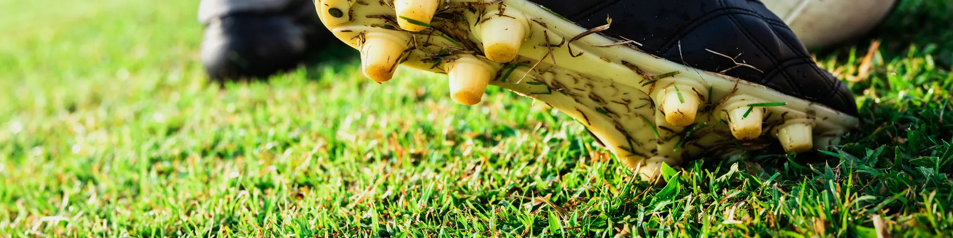 Ein Fussballer in roten Stutzen steht auf einem grünen Feld und bereitet sich darauf vor, einen Fussball mit dem schwarzen Schuh zu schiessen.
