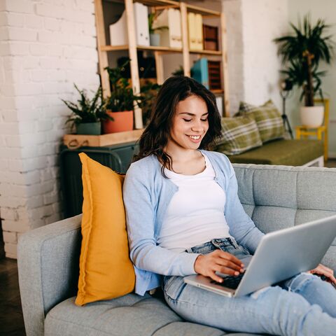 Junge Frau sitzt mit dem Laptop auf dem Sofa