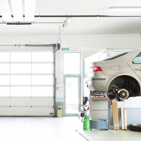 In a bright, tidy garage is a white car without wheels on the lift.
