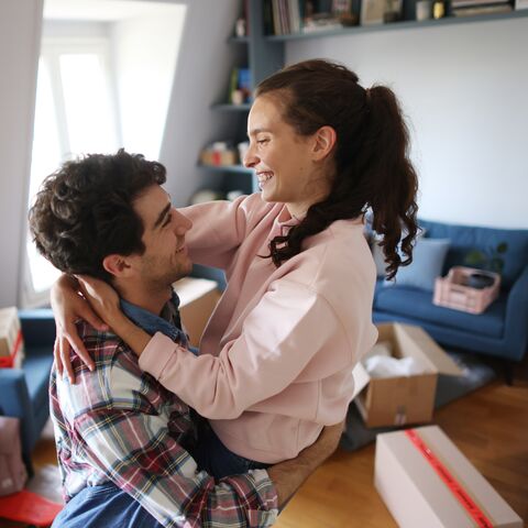 Un jeune couple est dans le salon et des cartons de déménagement sont visibles à l’arrière-plan.