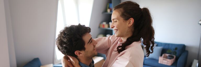 Un jeune couple est dans le salon et des cartons de déménagement sont visibles à l’arrière-plan.