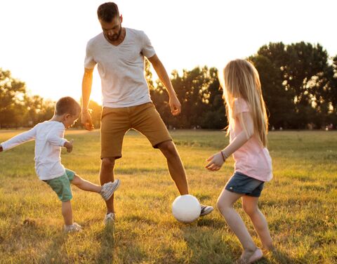 Un père joue avec son fils dans un champ ensoleillé, avec à côté des récompenses pour une assurance de premier plan et la première place pour les compléments d'assurance ambulatoires.