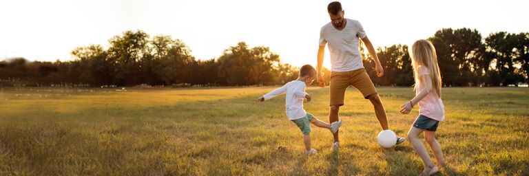 Un padre gioca con il figlio in un campo soleggiato dove vi sono anche riconoscimenti per un’assicurazione di prim’ordine e il 1° posto per i moduli complementari per prestazioni ambulatoriali.