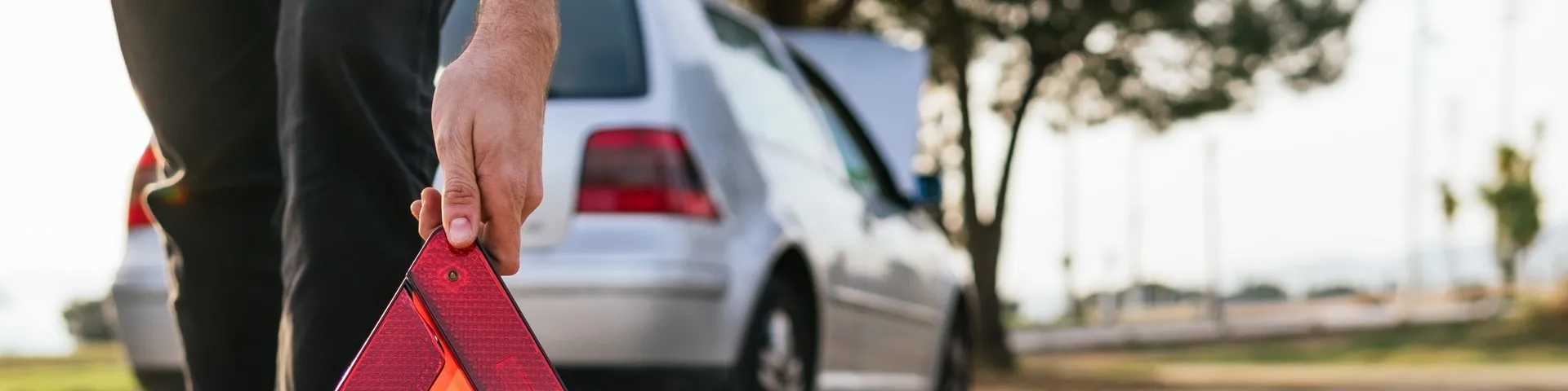 Ein rotes Warndreieck steht auf einer Strasse vor einem geparkten Auto, während eine Person daneben sichtbar ist.