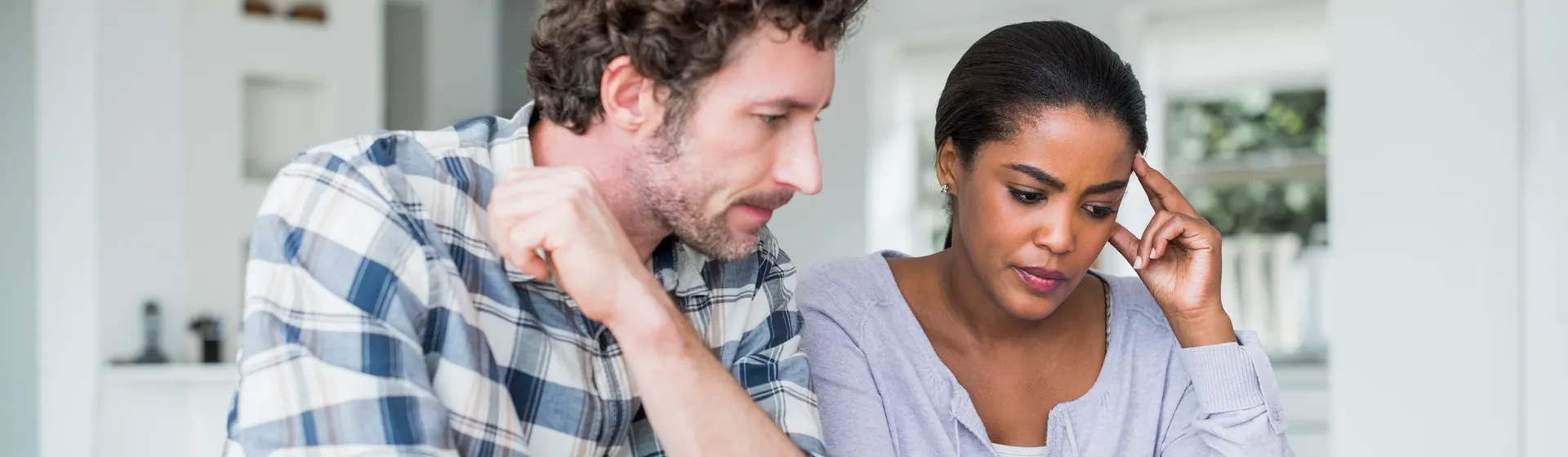 An anxious couple sits at a table, checking bills and discussing while the man holds a cup of coffee.
