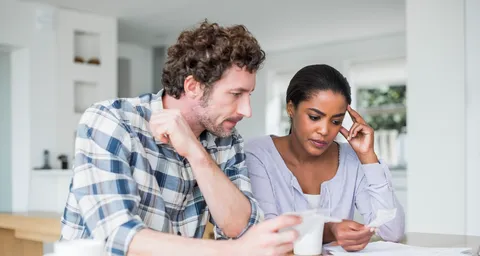 Un couple inquiet est assis à une table, vérifie les factures et discute pendant que l'homme tient une tasse de café.
