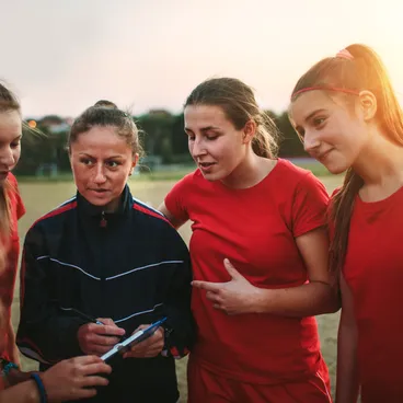 Un groupe de cinq jeunes femmes en tenue de sport se tient ensemble dans un champ et discute de quelque chose alors que le soleil se couche en arrière-plan.