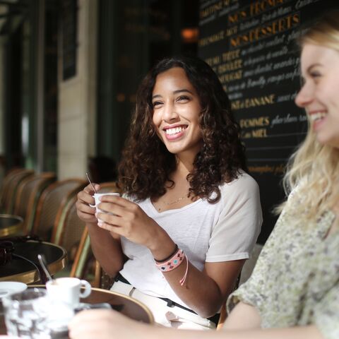 Deux jeunes femmes sont assises en riant devant une table de menu dans un café. Deux tasses à café sont posées sur leur table.