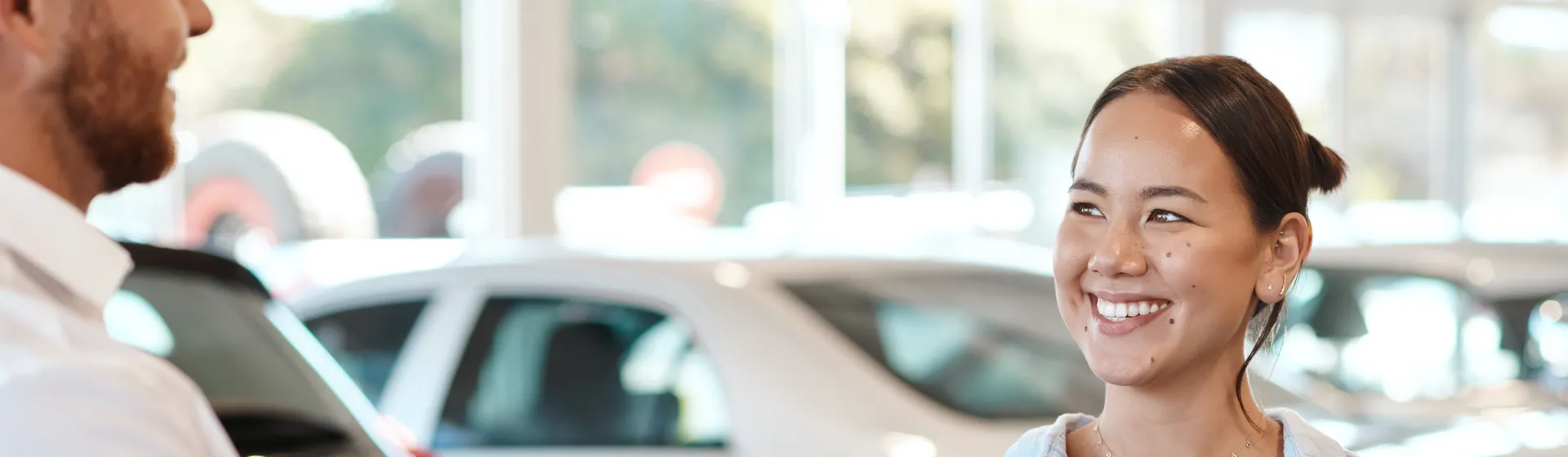 Una donna sorridente riceve la chiave di un'auto da un uomo in una concessionaria, mentre sullo sfondo sono parcheggiate diverse auto.