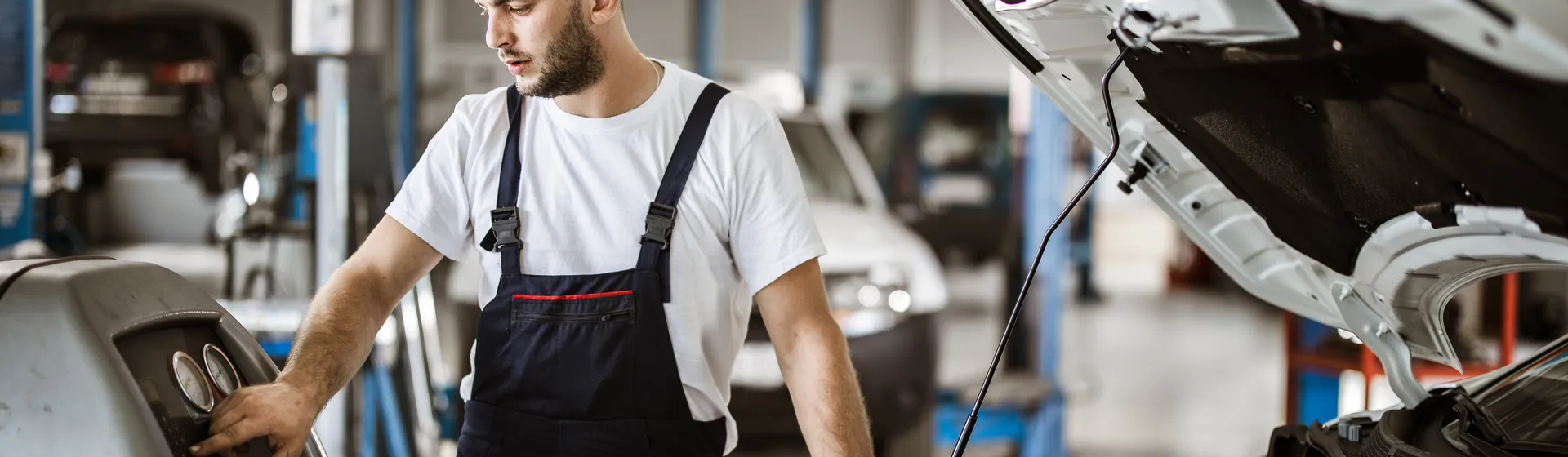 Un meccanico in tenuta da lavoro controlla un dispositivo diagnostico accanto a un'auto con il cofano aperto in un'officina.