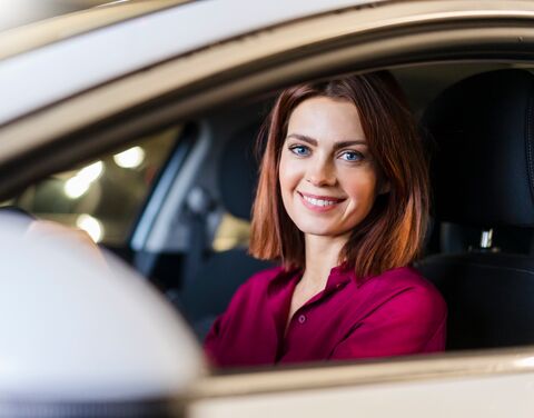 Frau mit blauen Augen und roten Haaren sitzt im Auto und lächelt.