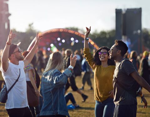 Vier Freunde tanzen an einem Festival. Im Hintergrund sieht man andere Festivalgänger und die Bühne.