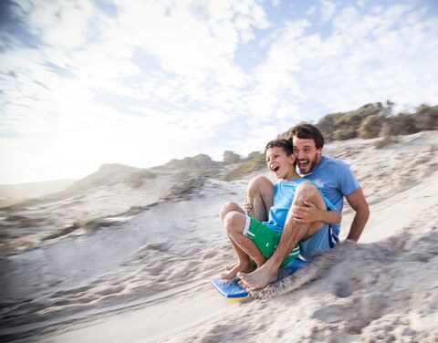 Ein Vater und sein Sohn schlitteln auf einer Sanddüne.