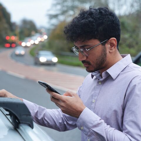 Un giovane uomo ferma sul ciglio della strada accanto alla sua auto e guarda lo smartphone.
