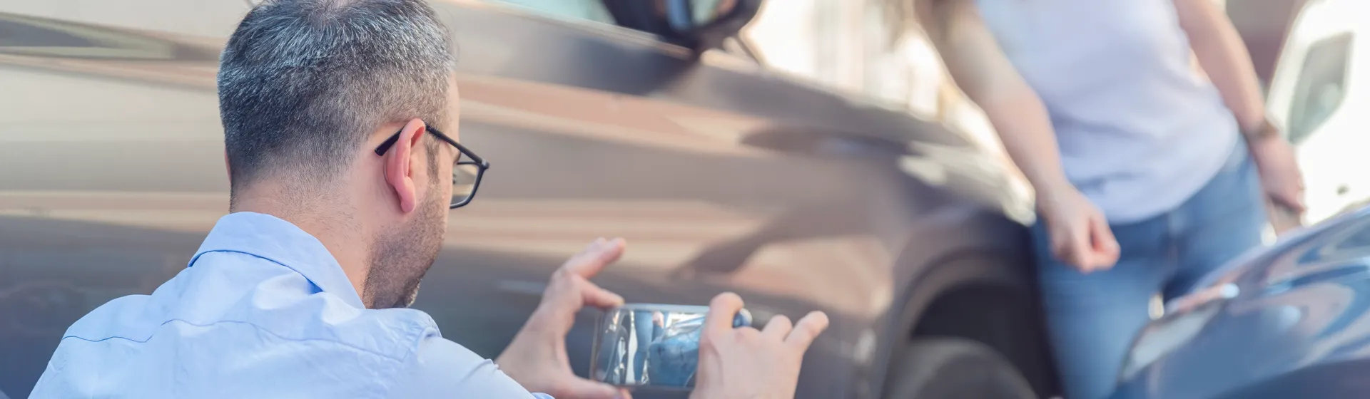 Un jeune homme se tient au bord de la route à côté de sa voiture et regarde son smartphone.