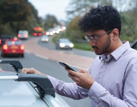 Un giovane uomo ferma sul ciglio della strada accanto alla sua auto e guarda lo smartphone.