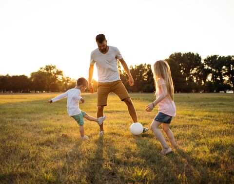 Un père joue avec son fils dans un champ ensoleillé, avec à côté des récompenses pour une assurance de premier plan et la première place pour les compléments d'assurance ambulatoires.